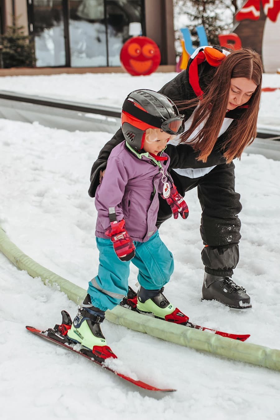 Kleines Kind lernt mit Hilfe eines Skilehrers Skifahren bei der Kinderskischule Kleinarl